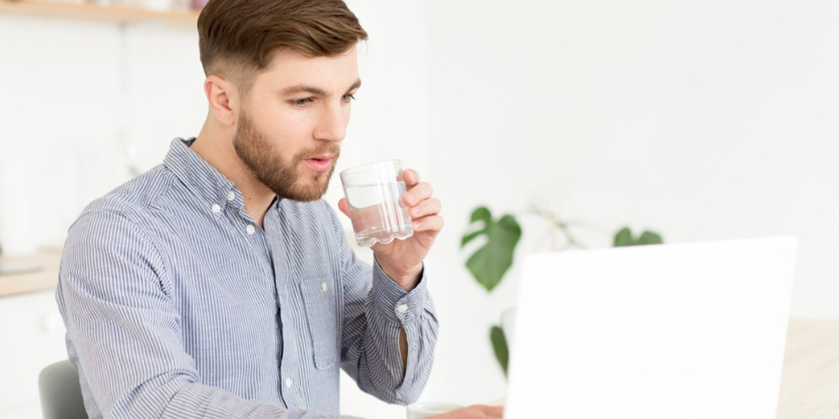 Man drinking clean water while on laptop because his office manager understands the importance of water filtration